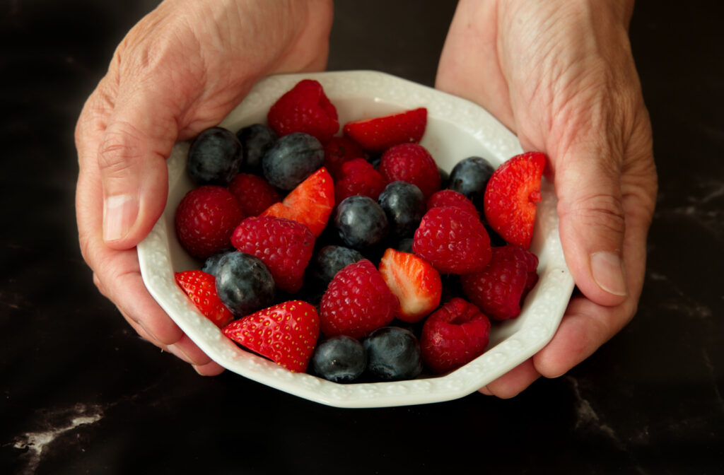 A senior woman's hands holding a bowl of blueberries and strawberries.