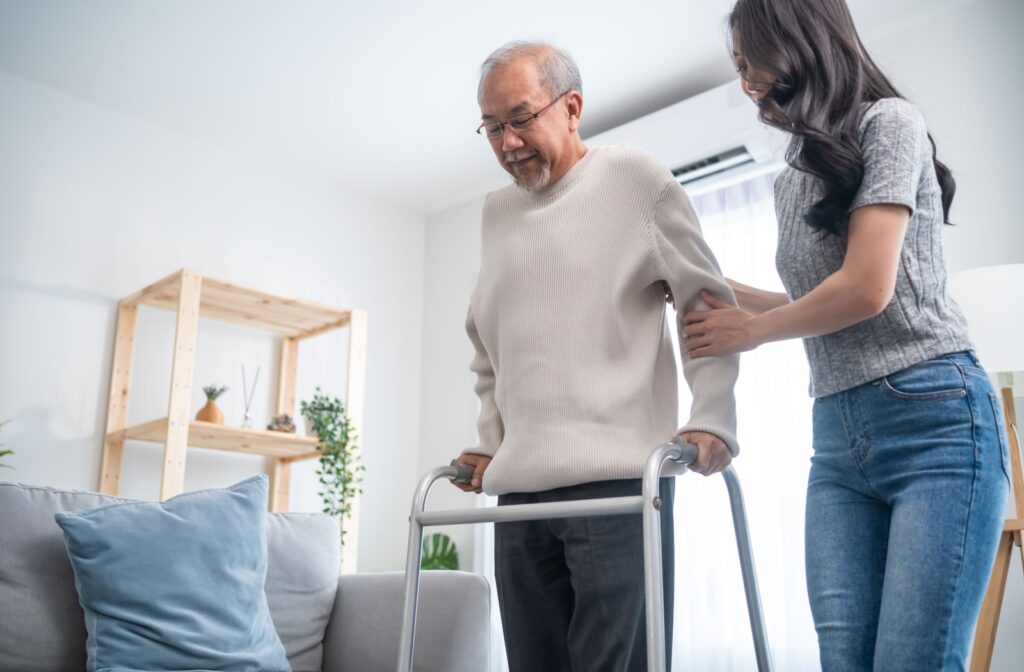 An adult child supports their elderly father walk with a walker in the home.